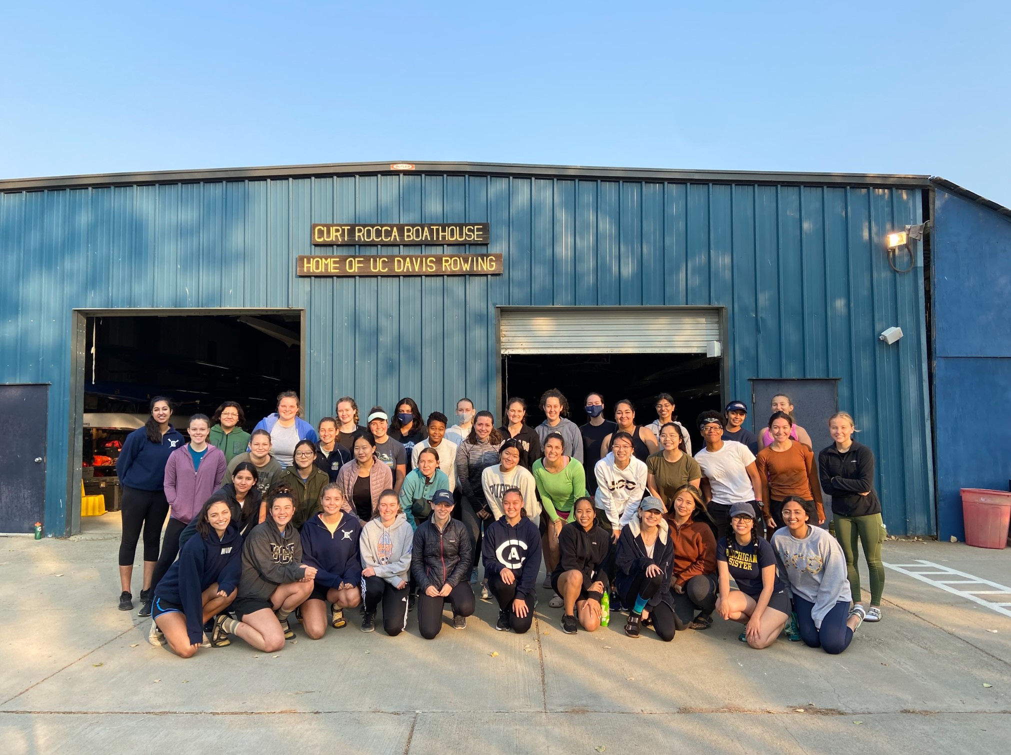 Approximately 35 UCD rowers standing in front of Curt Rocca Boathouse