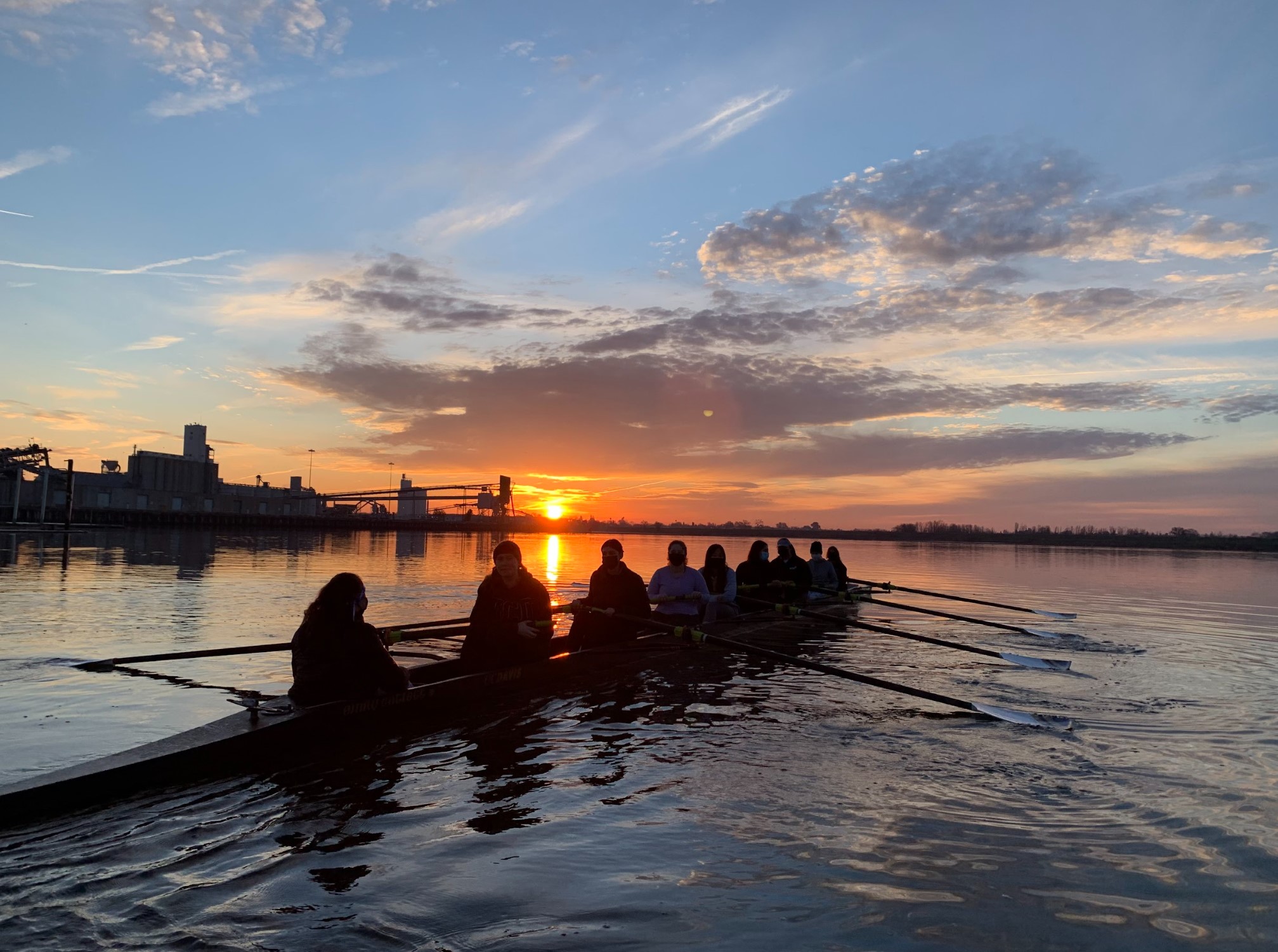 The silhouette with a coxswain and eight rowers against a sunrise