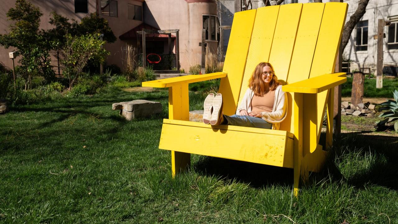 Image of a student sitting in an oversized yellow Adirondack chair on a grassy lawn