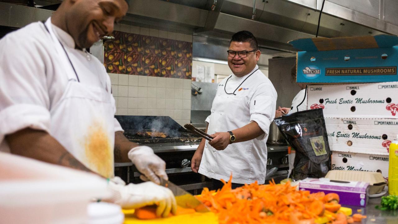 Chef Freddie Bitsoie cooks at grill while sous chef chops vegetables