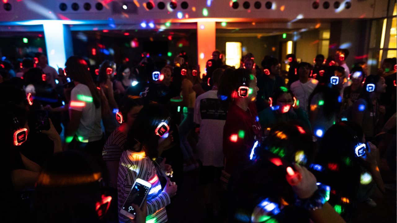 Room full of students at silent disco with multicolored lights and headsets