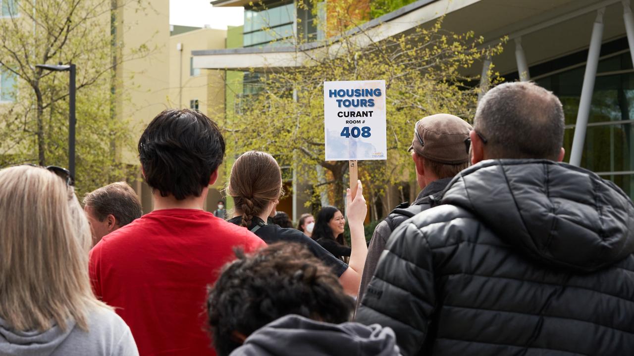 Housing tour group from behind.  Tour guide holding up a sign that reads "Housing Tours Currant Room #408"