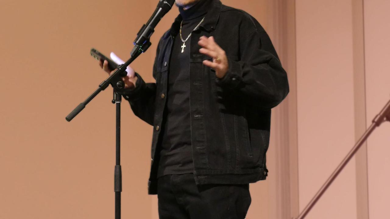 A young spoken word artist wearing a cap speaks into a microphone. 