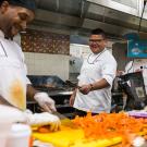 Chef Freddie Bitsoie cooks at grill while sous chef chops vegetables