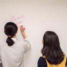 Two students write debate and other words on a whiteboard.