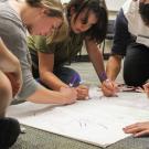 group of students writing with markers on large sheet of paper on the floor